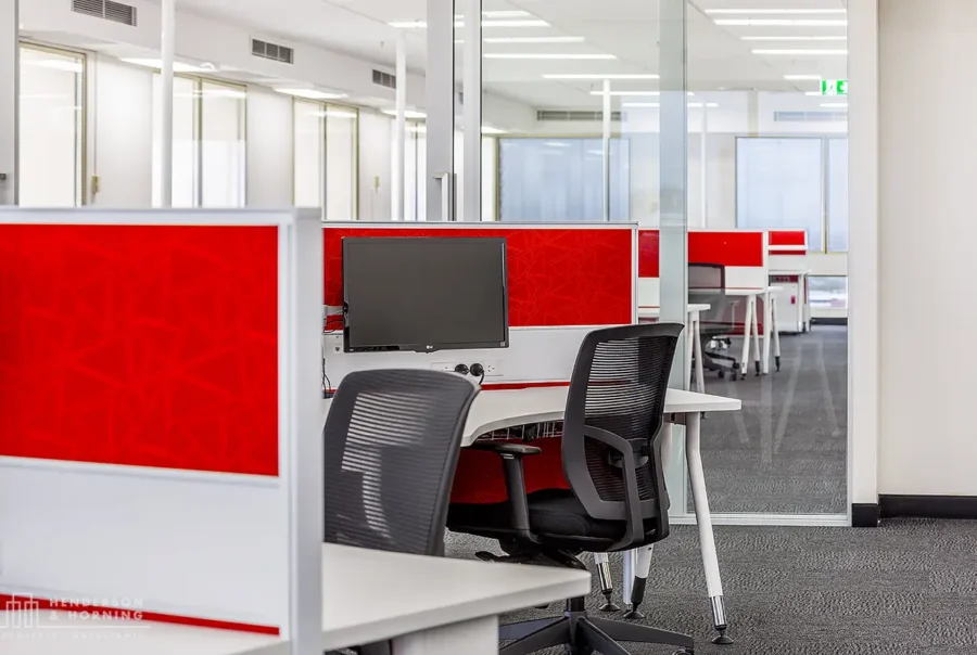 An office space with red and white partitioned desks, black office chairs, and computer monitors.