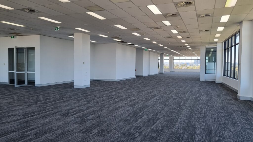 Empty modern office space with suspended ceiling, white partition walls, and large glass windows providing natural light.