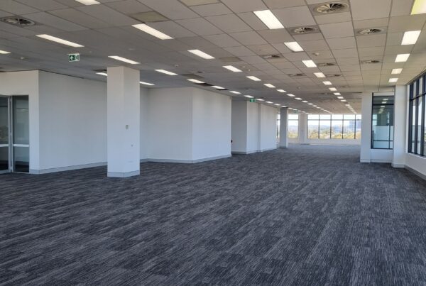 Empty modern office space with suspended ceiling, white partition walls, and large glass windows providing natural light.