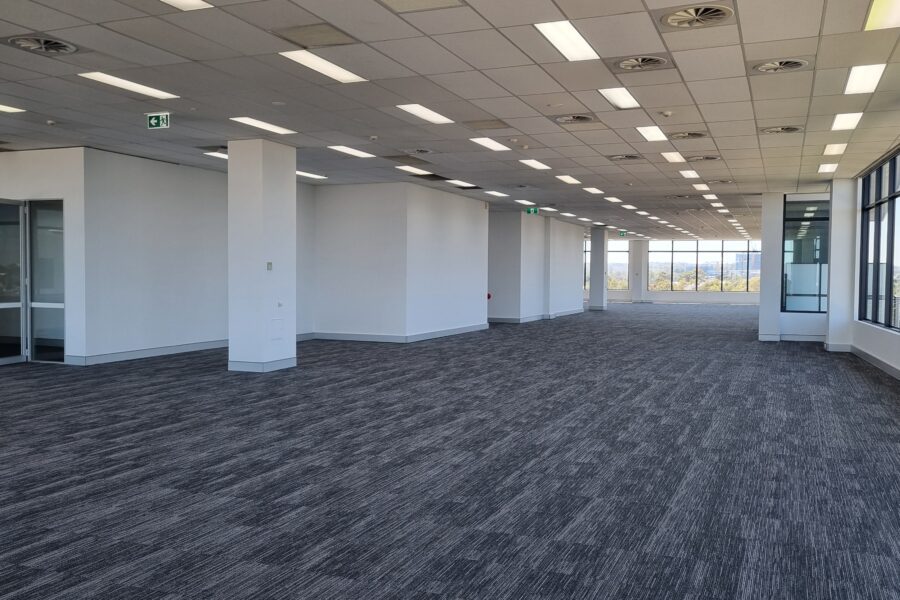Empty modern office space with suspended ceiling, white partition walls, and large glass windows providing natural light.