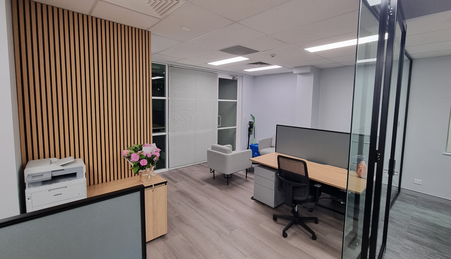 Modern open-plan office at Medicines R Us in Norwest featuring timber slat wall panelling, workstations, glass-partitioned offices, lounge seating, and contemporary office furniture.