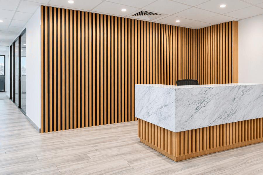 Modern reception area in Norwest Business Park featuring a marble-look reception desk, timber wall panelling, timber batten detailing, and contemporary commercial office design.