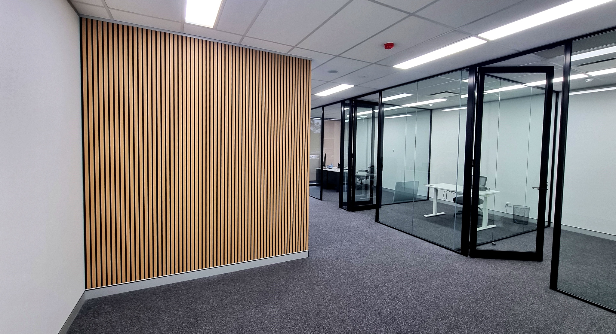 Modern reception area in Norwest Business Park featuring a black reception desk, illuminated timber slat wall panelling, contemporary office finishes, and a professional commercial office fitout.